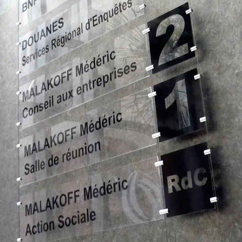 Photo de panneaux directionnels en plexiglass montés sur des cables avec entretoises inox dans le hall d'un immeuble d'affaires